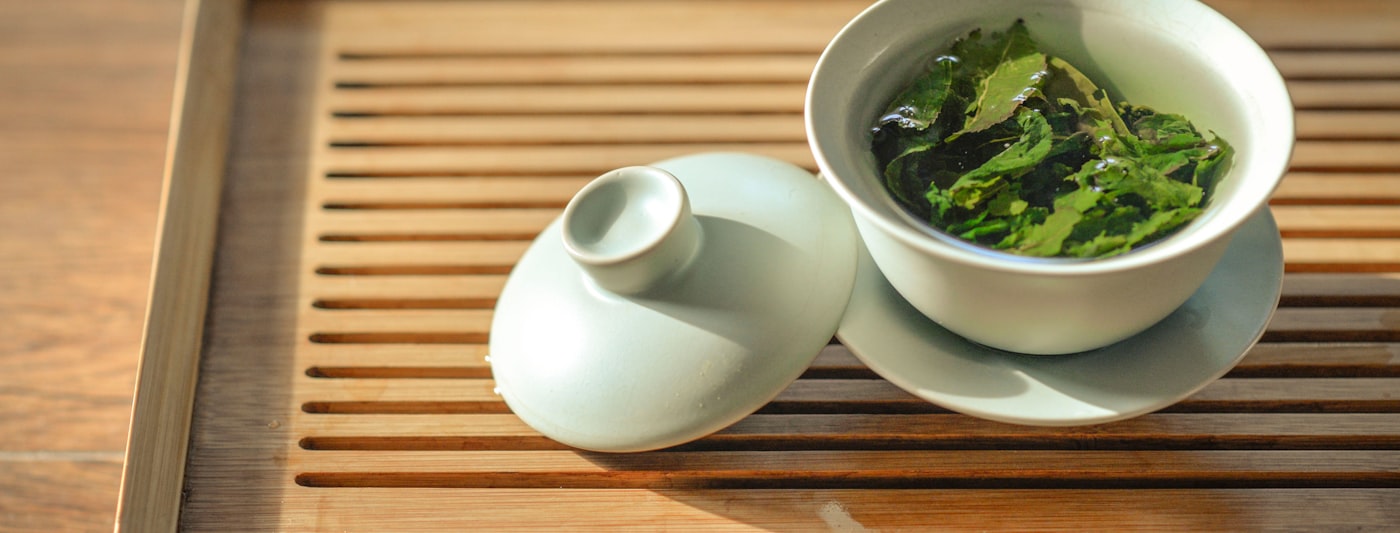 Loose green tea leaves in a white ceramic bowl
